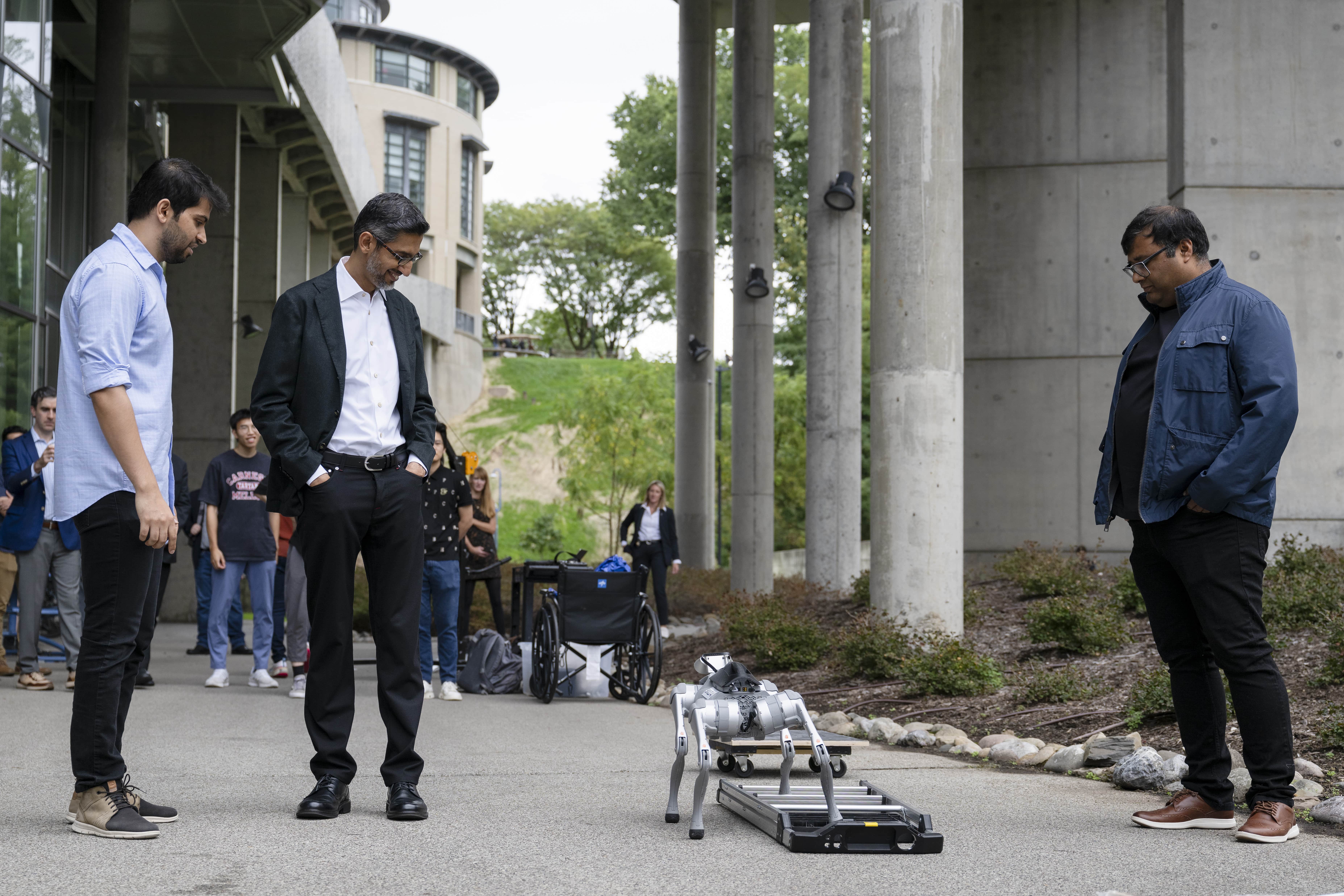 Pathak (left) and Abhinav Gupta, faculty member in The Robotics Institute and co-founder of Skild AI (right), join Pichai in watching a robot adapt to changing terrain.