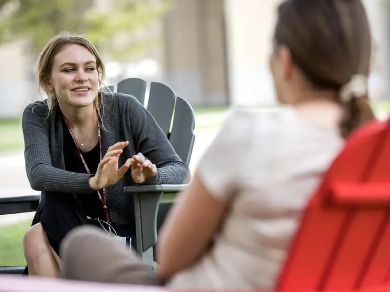 Two continuing education students sit on chairs outdoors on CMU's campus, engaging in discussion