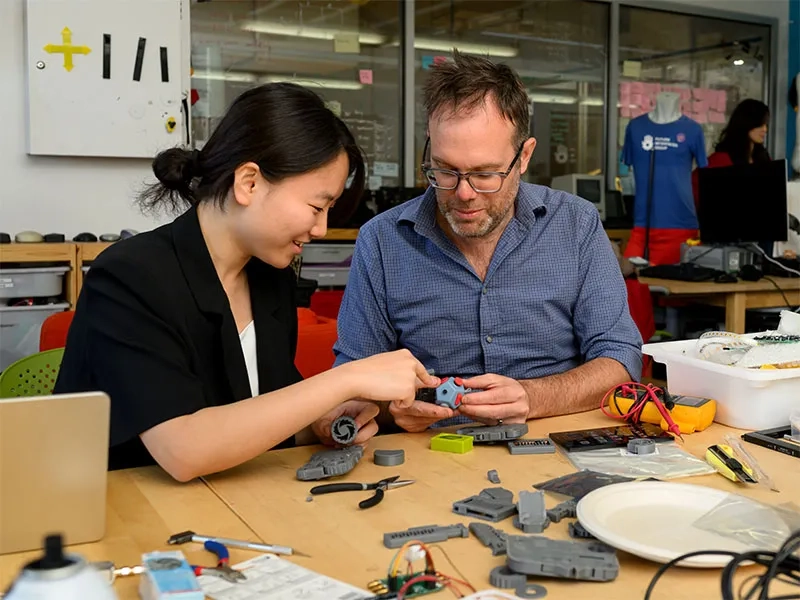 Student and professor, working at a table on the physical component to an AI project.