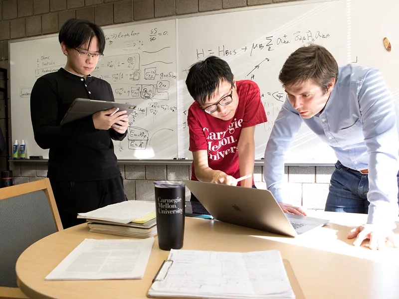 Three CMU graduate students work on a whiteboard. 