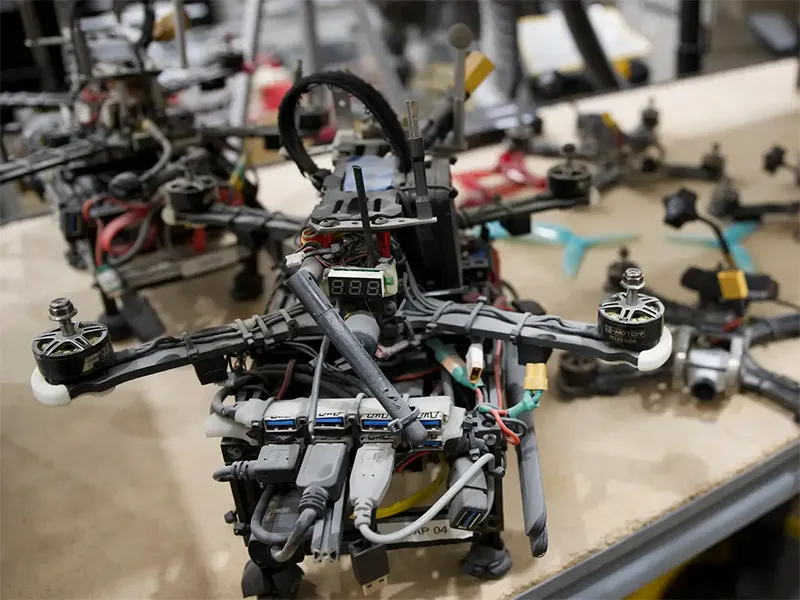 A drone sitting on a work table, with other drones being built on the same table.