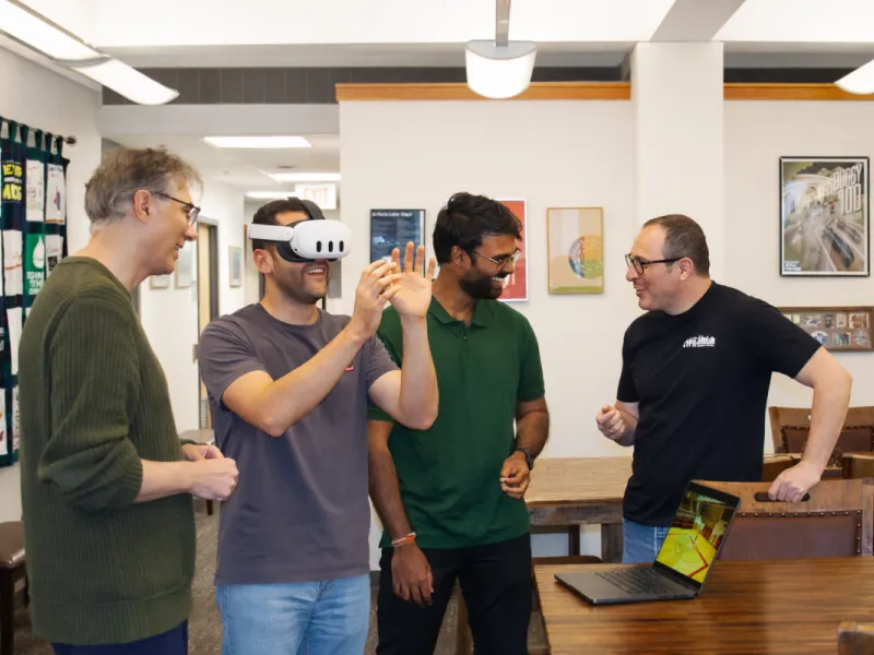 Several people standing and smiling near someone wearing virtual reality goggles