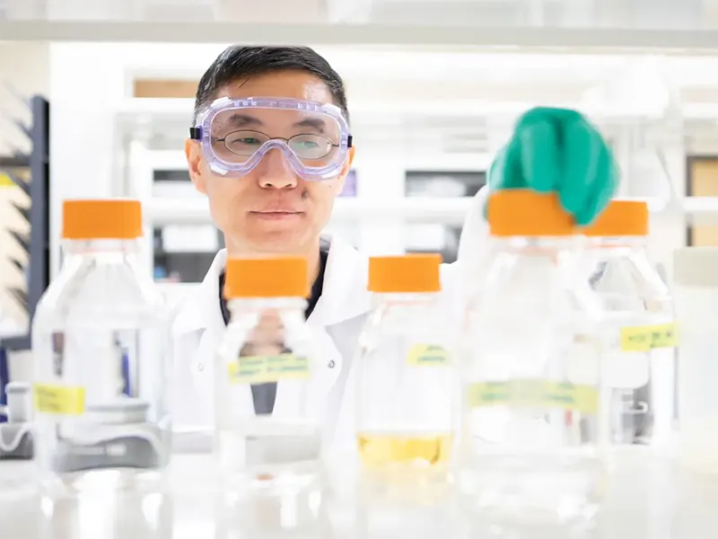 Fangwei Si in a lab, looking at labeled bottles.