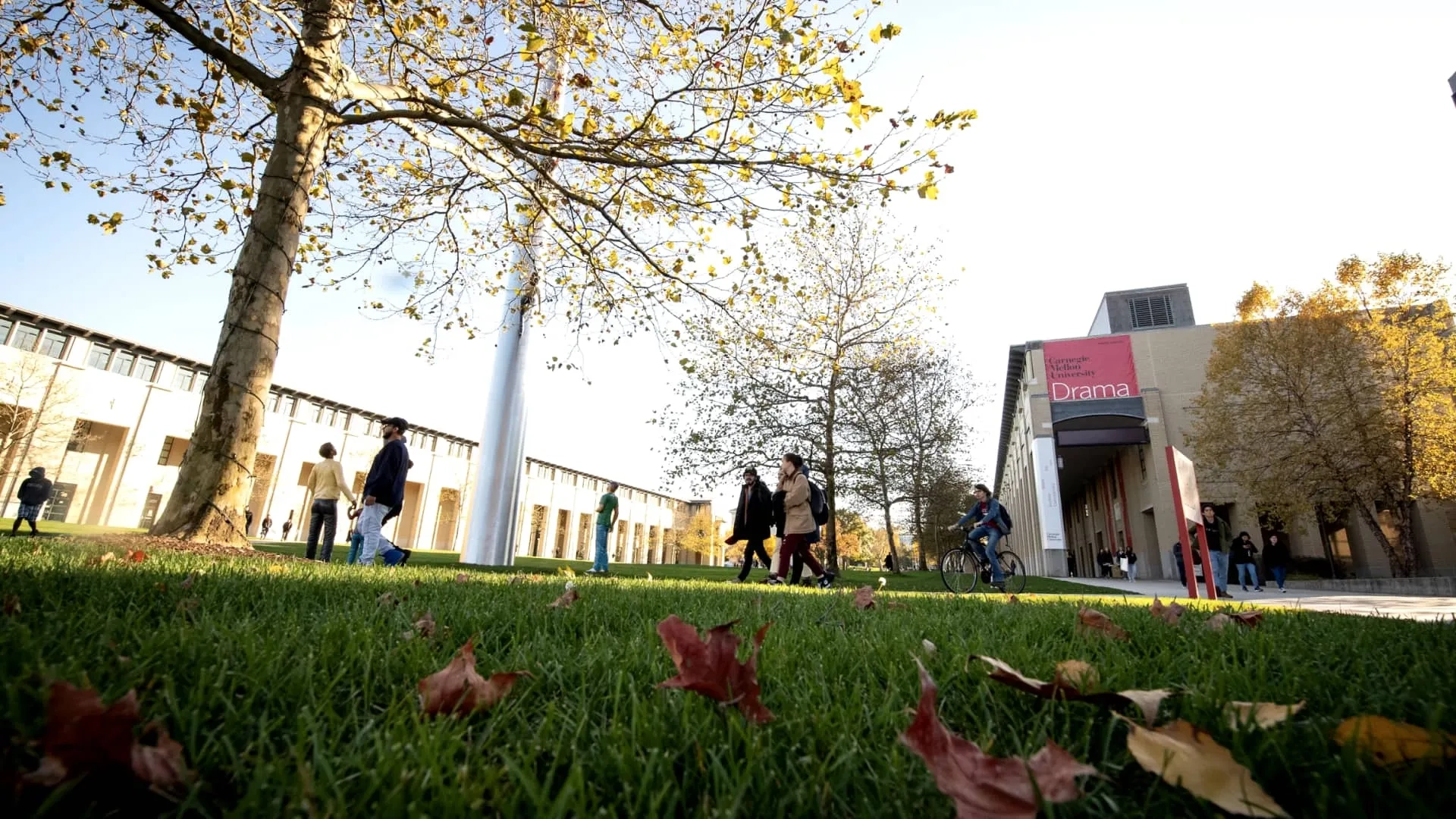 Students walk and bike through the green space between academic buildings on Carnegie Mellon University's campus on a sunny day