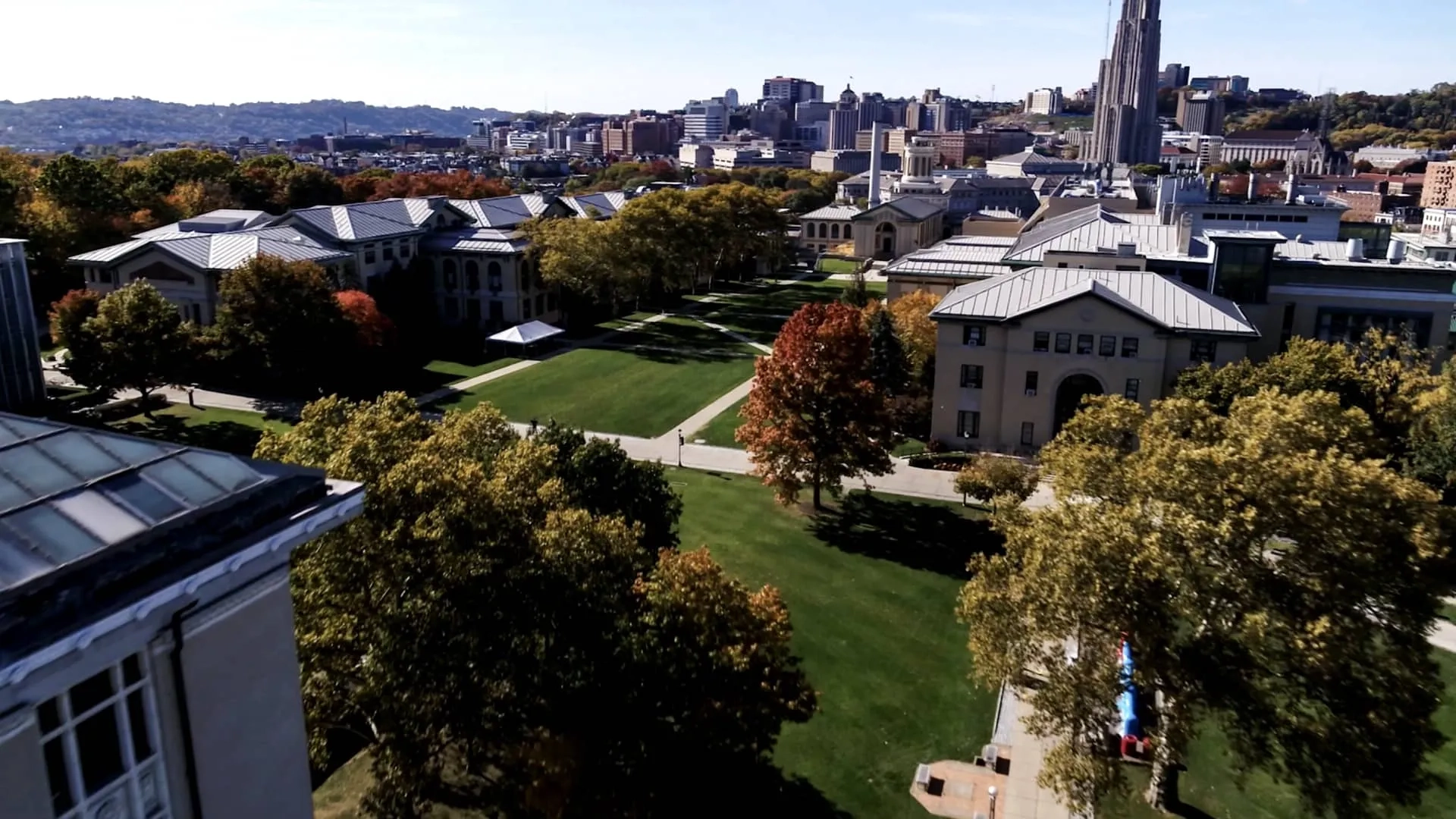 Aerial view of CMU's campus with green lawns and tree-lined paths and the Pittsburgh cityscape in the background