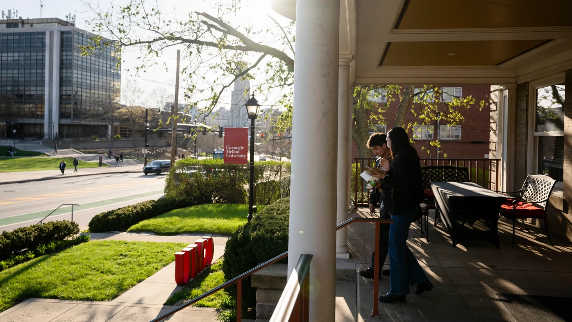 Two students walk down the front porch steps of the Alumni House.
