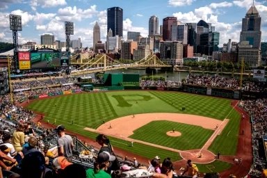 Aerial view of PNC Park during a Pittsburgh Pirates baseball game, with the Pittsburgh skyline and yellow bridges as a scenic backdrop