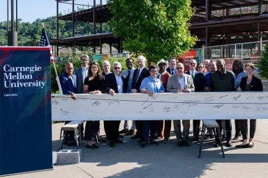CMU leadership standing in front of a signed I-beam at the Robotics Innovation Center at Hazelwood Green.